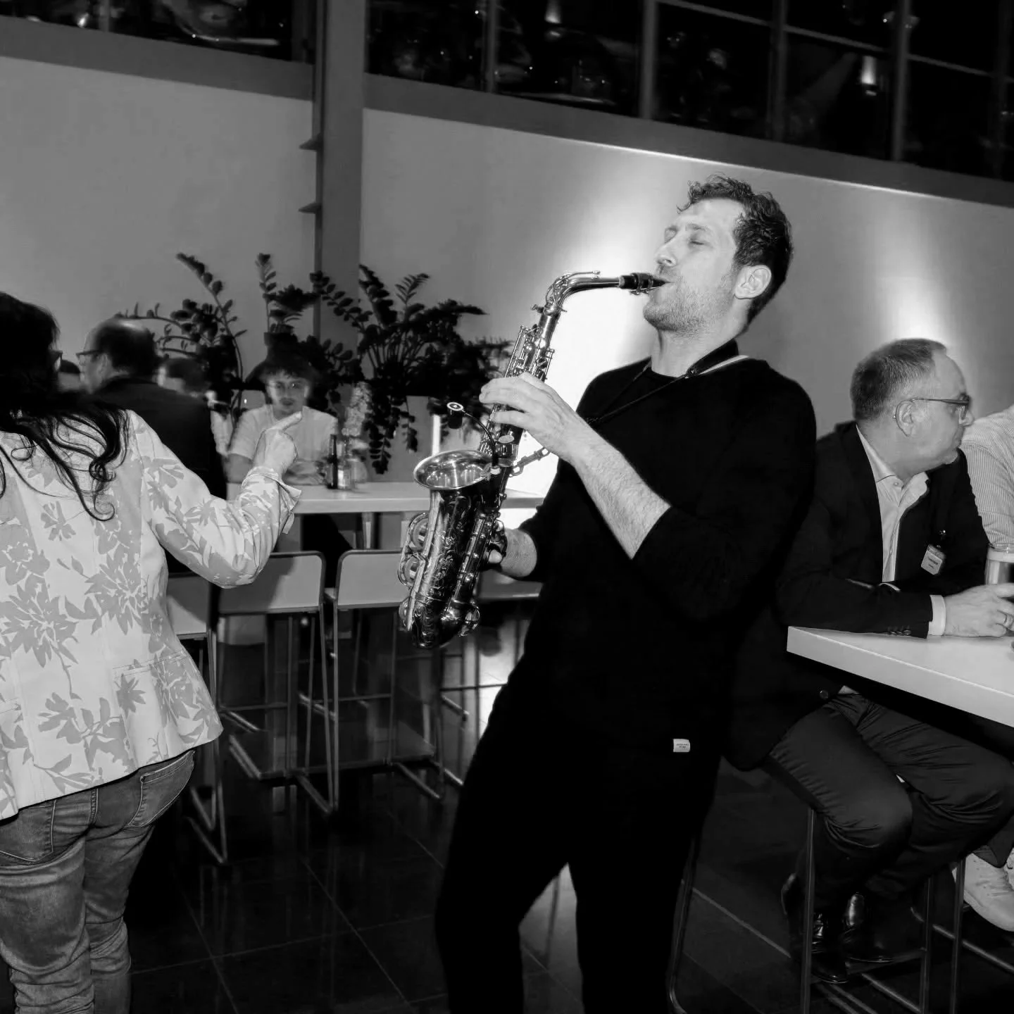 Frederik Heckel spielt Saxophon in einer Bar, im Hintergrund sitzen andere Gäste und unterhalten sich.