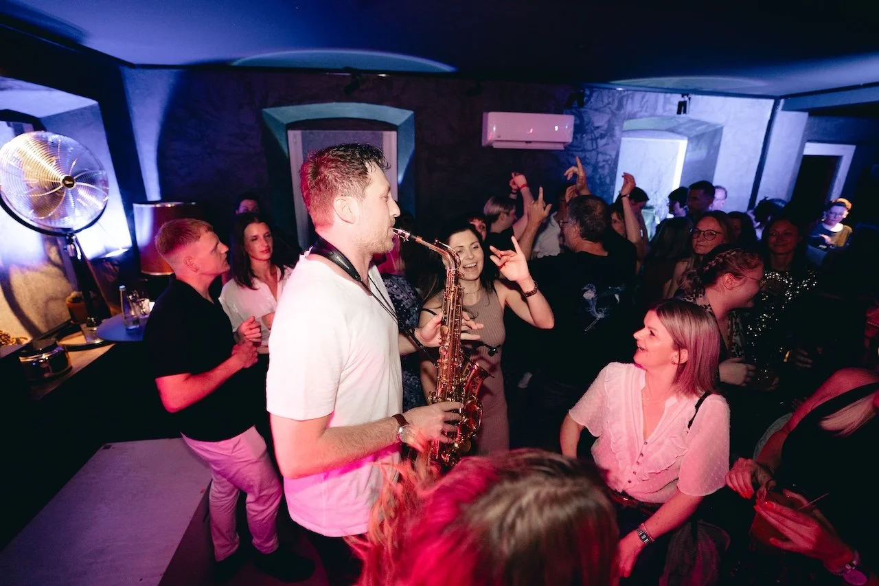 Menschen tanzen und feiern in einer Party mit einem Saxophonspieler im Mittelpunkt.