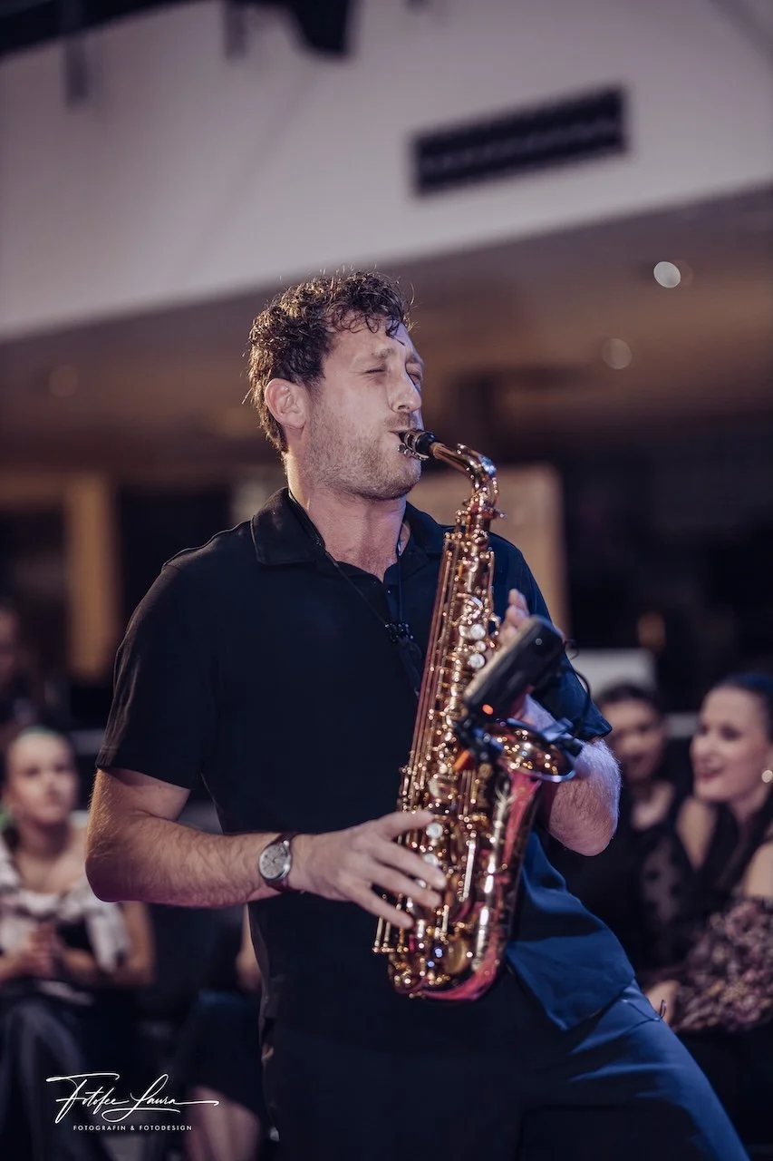 Frederik Heckel spielt Saxophon in einer Gruppe, im Hintergrund sind mehrere Frauen, die zuhören.