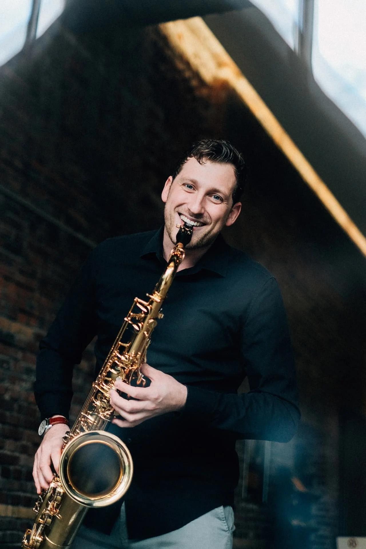Frederik Heckel spielt Saxophon in einem dunklen Raum mit einer Backsteinwand im Hintergrund.