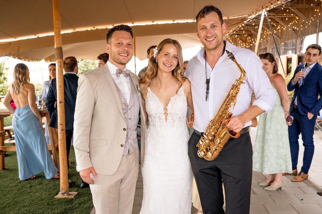 Frederik Heckel als Live-Saxophonist und Menschen feiern bei einer Hochzeit, mit Musik und festlicher Kleidung, unter einem Zelt mit Lichterketten.