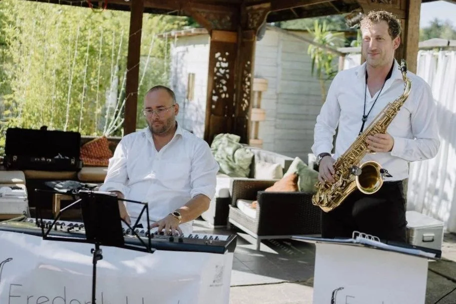 Zwei Musiker spielen im Freien. Einer sitzt und spielt ein Keyboard, der andere steht und spielt Saxophon.