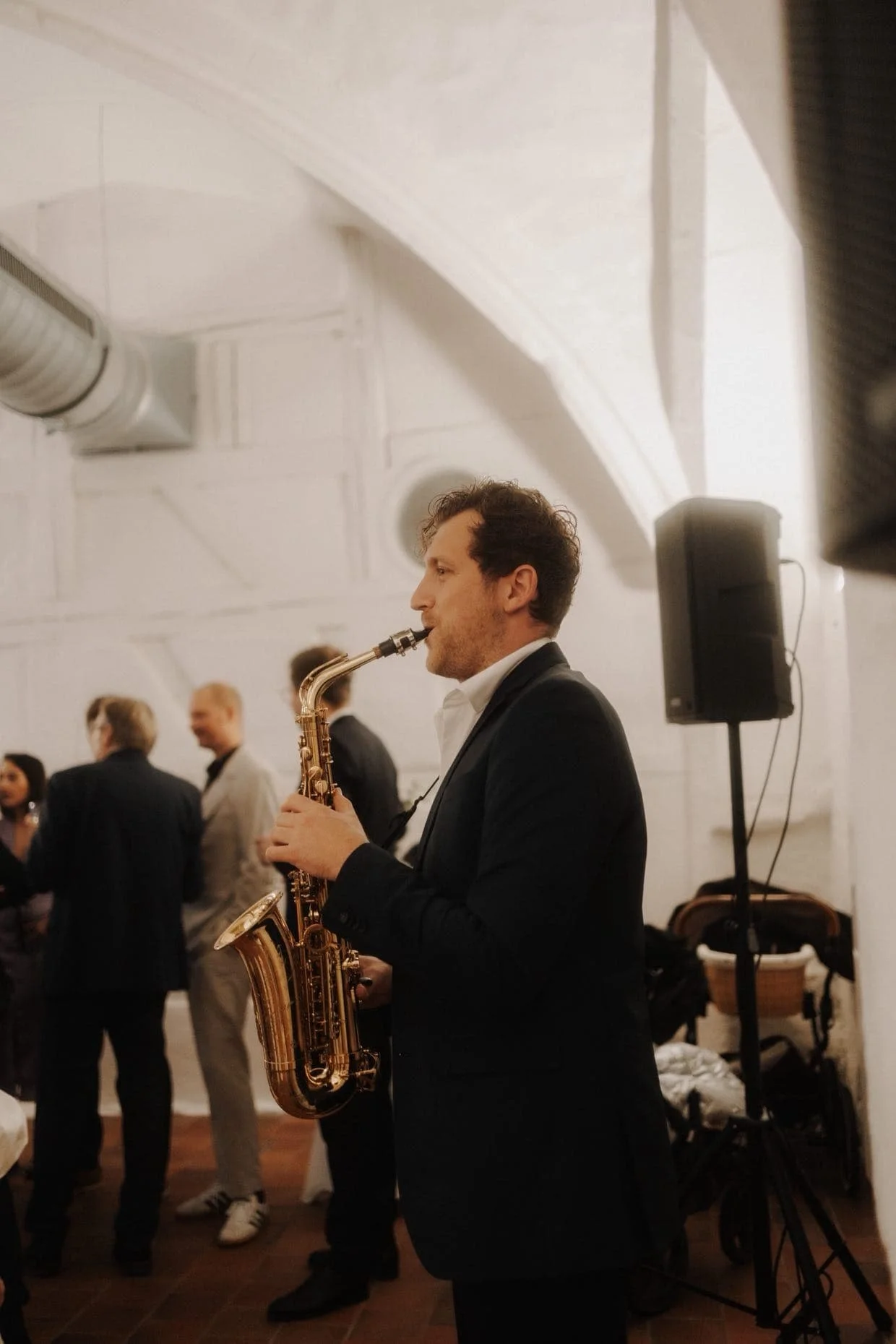 Frederik Heckel in formeller Kleidung spielt ein Saxophon bei einer Veranstaltung in einem festlich dekorierten Raum.