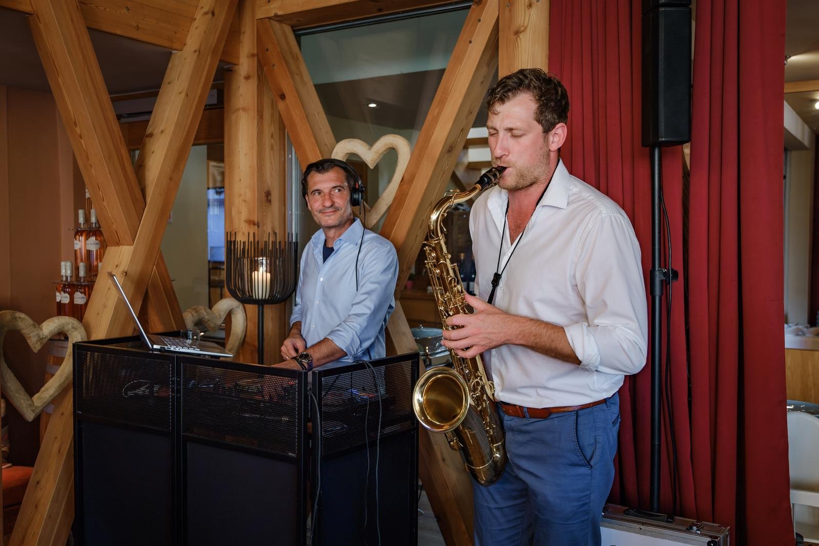 Zwei Männer, die Live-Musik in einem Raum mit Holzwanddekoration spielen. Einer spielt Klavier, der andere spielt Saxophon.
