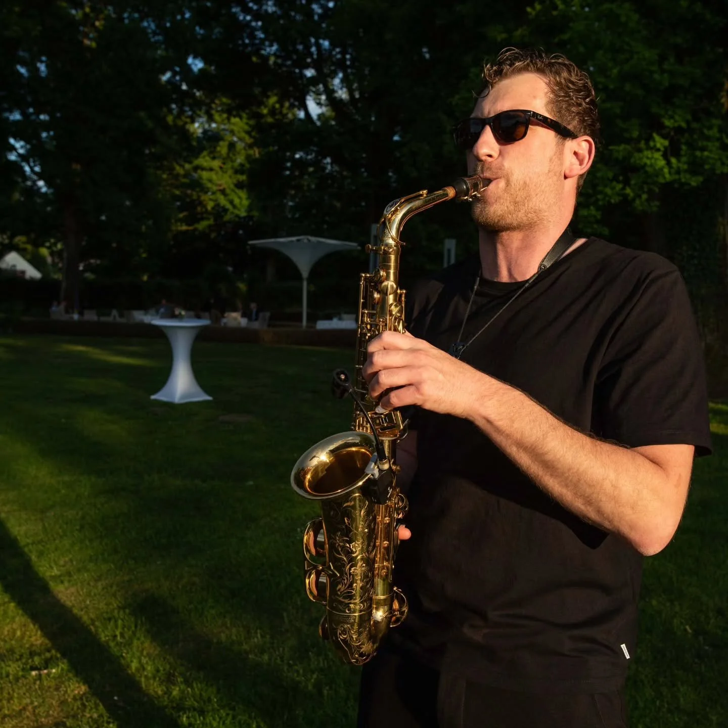 Frederik Heckel spielt Saxophon im Freien bei Sonnenuntergang, trägt schwarze Kleidung und Sonnenbrille.