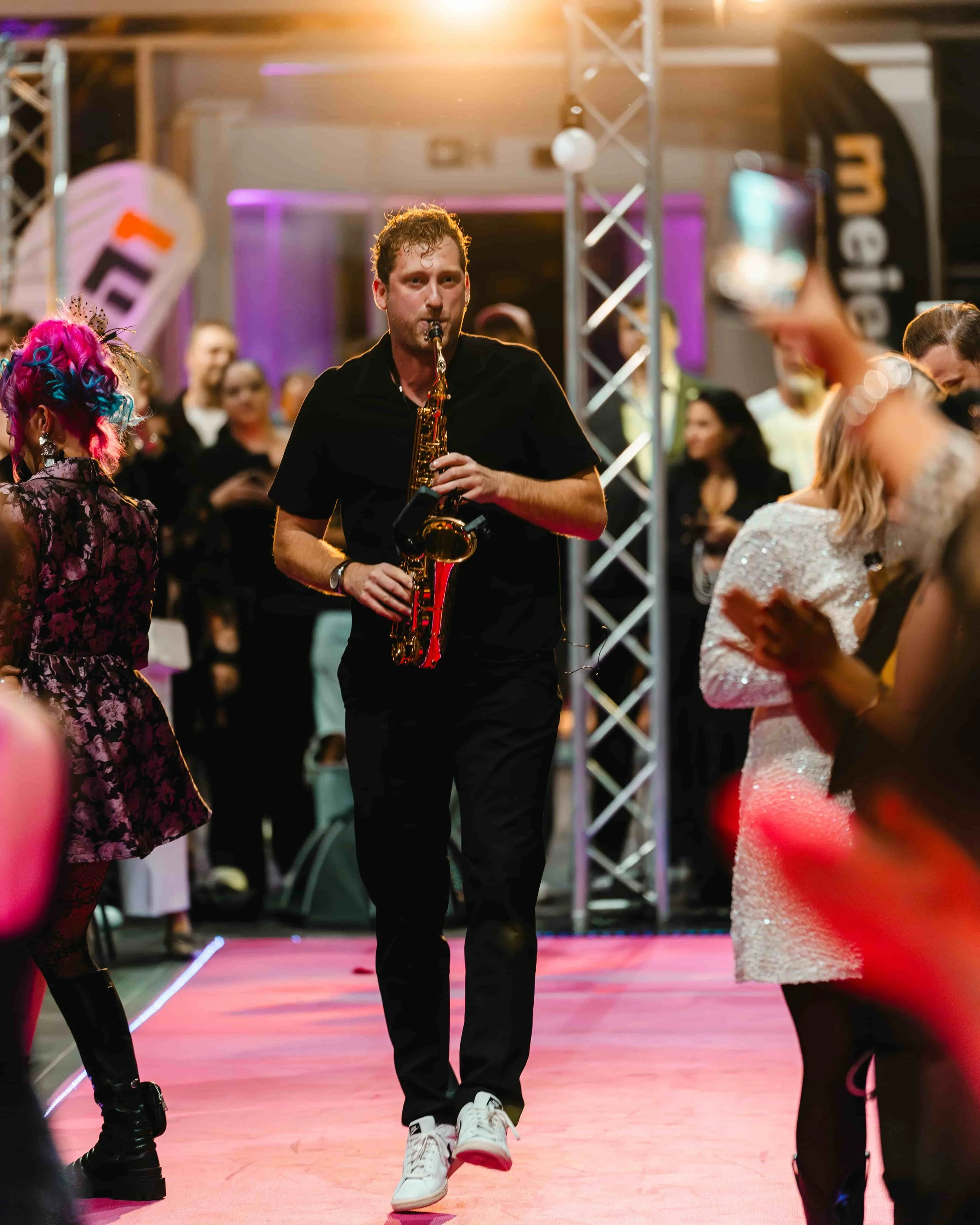 Frederik Heckel spielt Saxophon auf einer Party mit Menschen, die tanzen und klatschen, bunte Beleuchtung im Hintergrund.