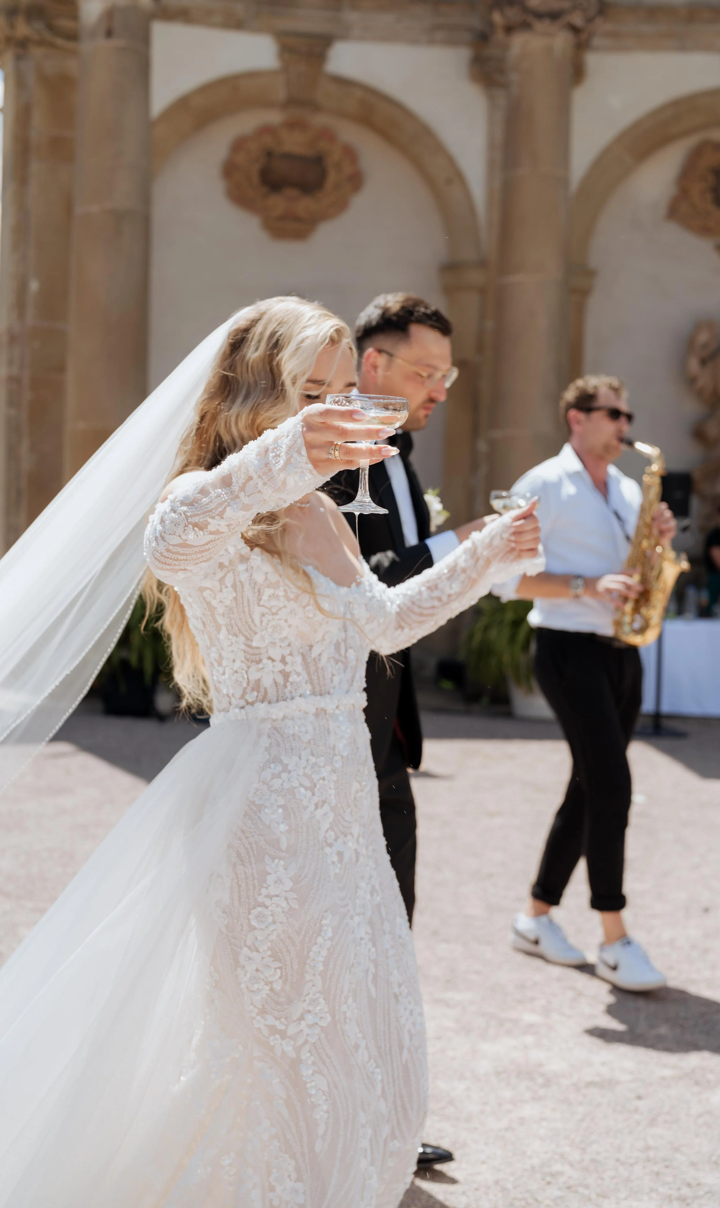 Hochzeitspaar in traditioneller Kleidung mit Frederik Heckel im Hintergrund, der Saxophon spielt, bei einer Hochzeitsfeier im Freien.