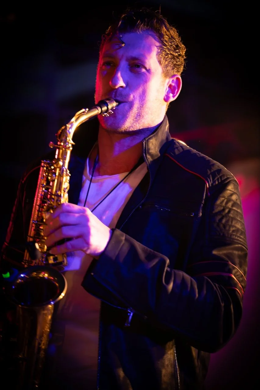 Frederik Heckel spielt Saxophon auf einer Bühne bei schwachem, farbigem Licht.