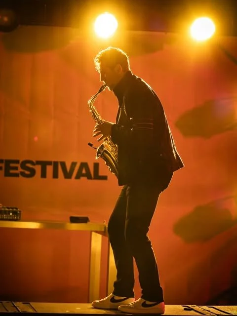 Frederik Heckel spielt Saxophon auf einer Bühne mit gelben Scheinwerfern im Hintergrund.