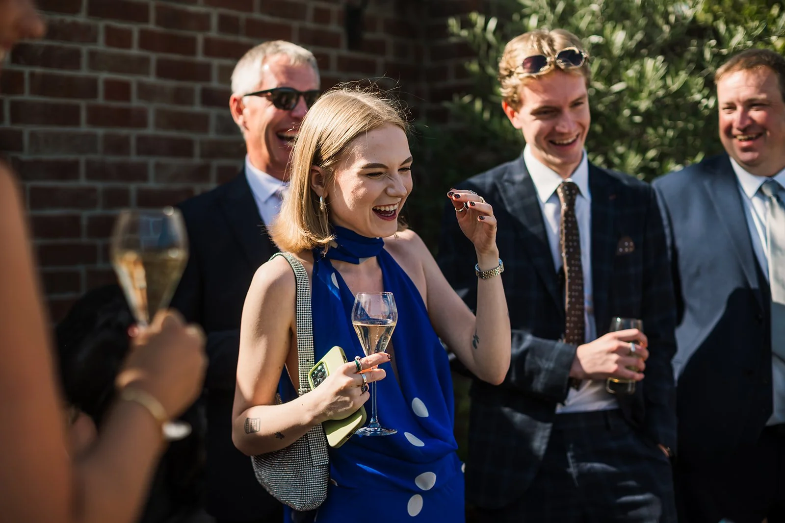 Wedding guests laughing during close-up magic performance at outdoor reception