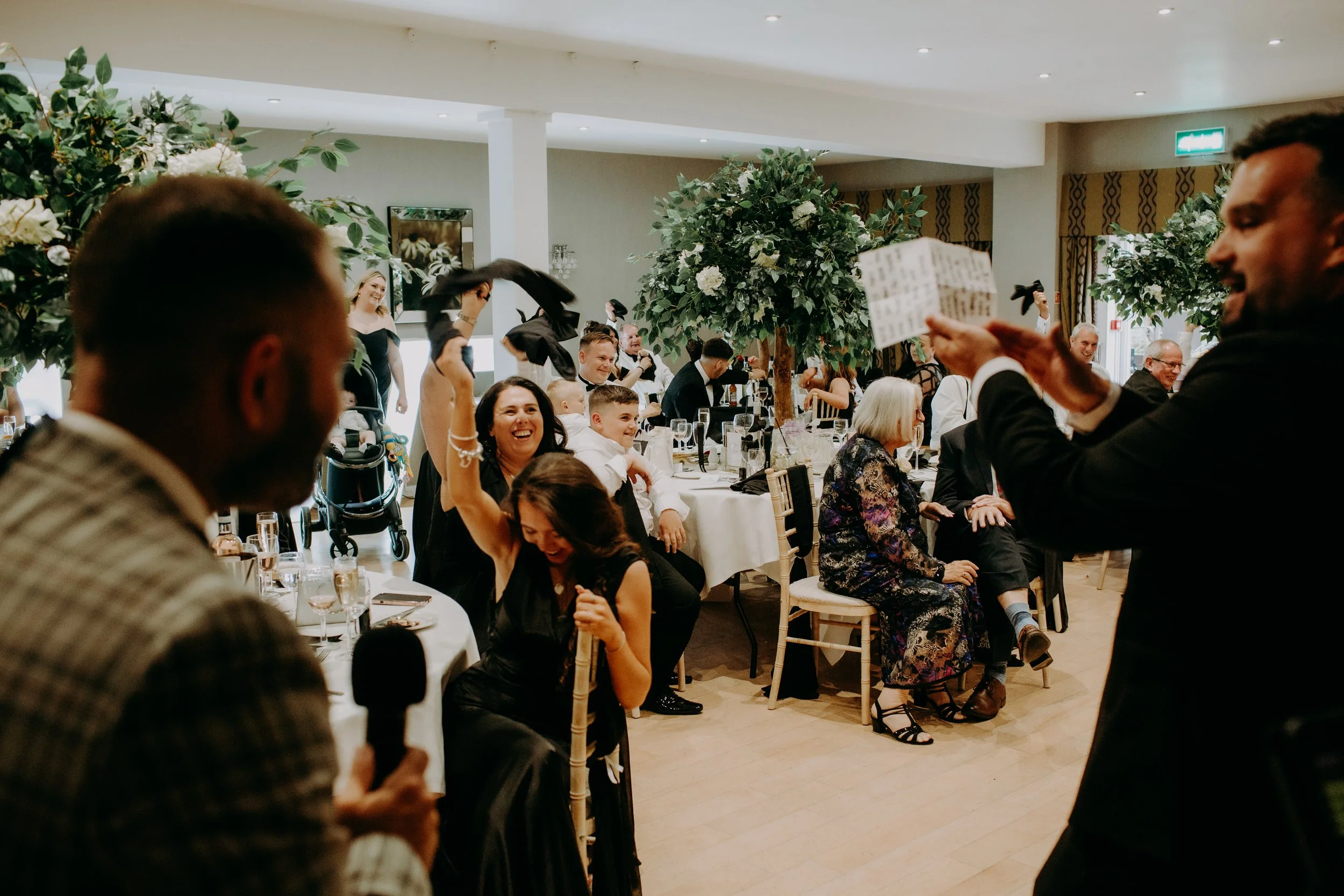 Wedding guests waving napkins during after-dinner magic show in reception room.