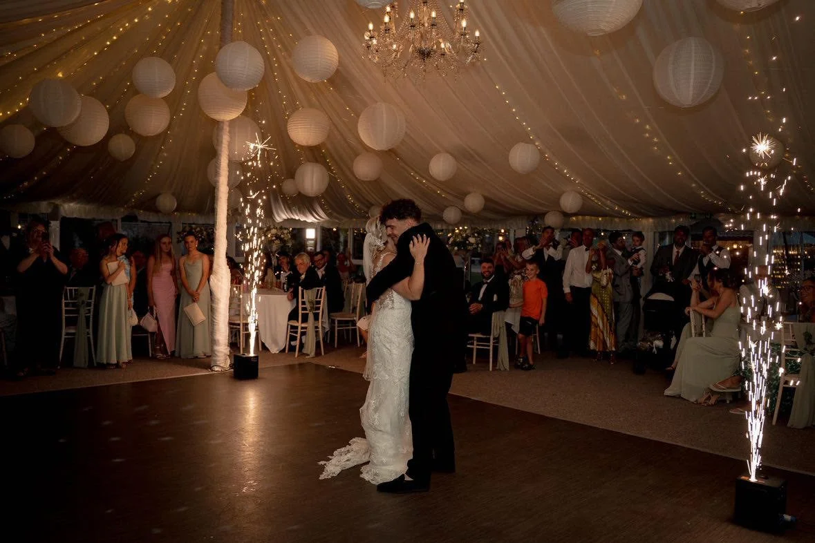 Bride and groom first dance under fairy lights with cold spark effects at a marquee wedding reception