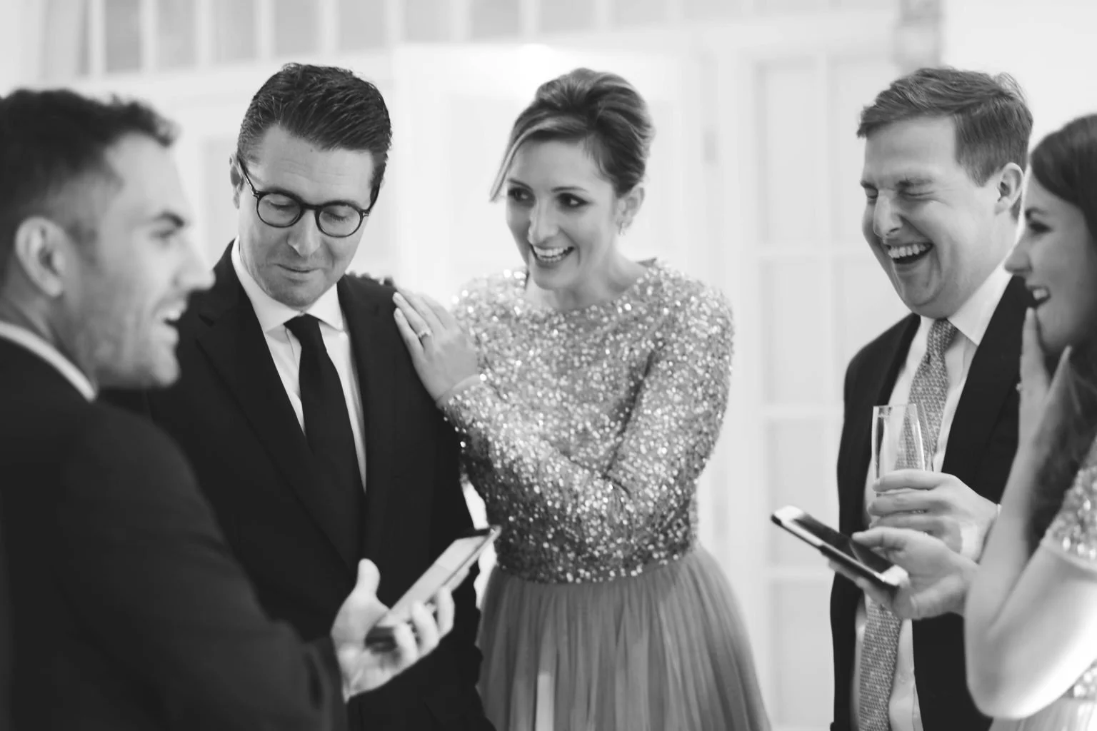 Wedding magician performing close-up magic for smartly dressed guests in a black and white photograph