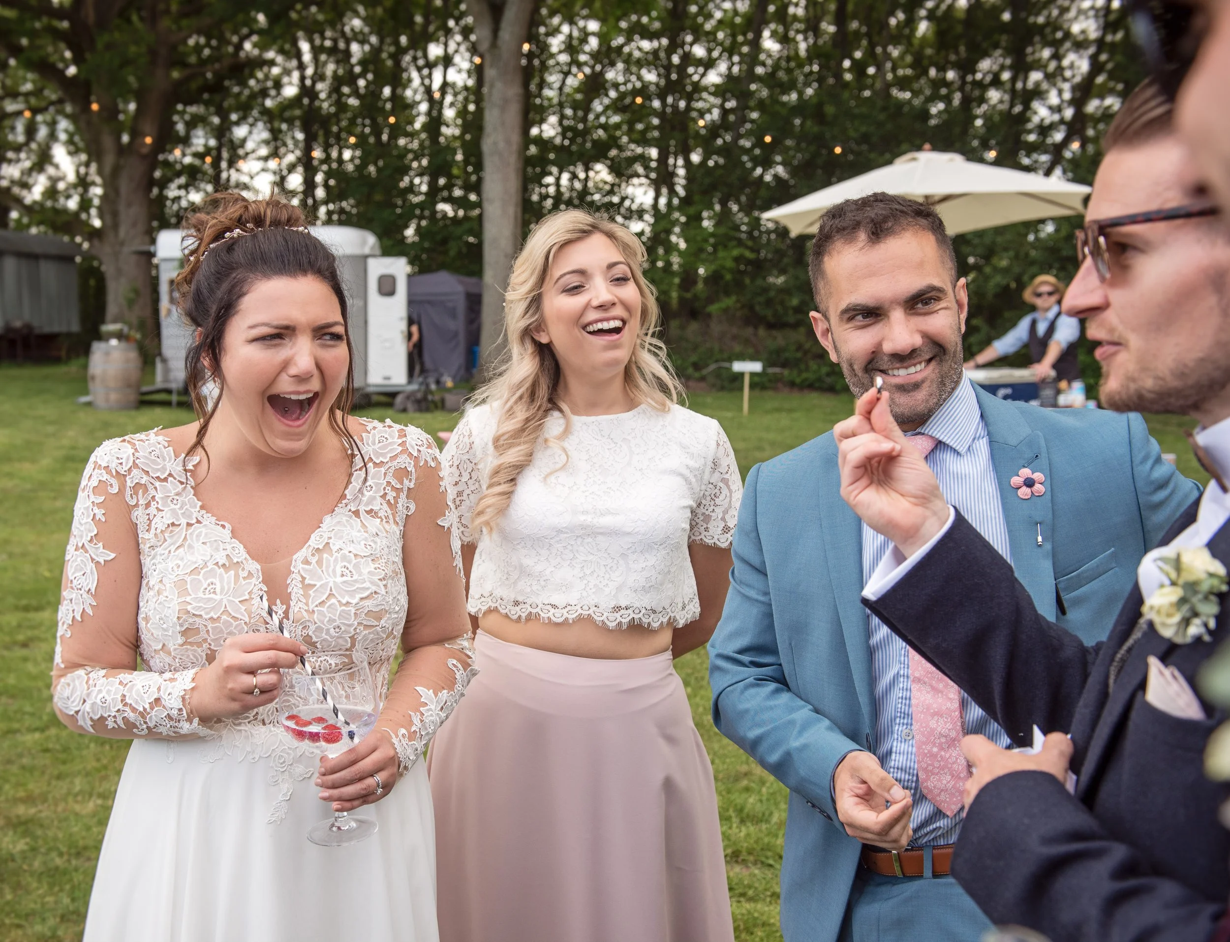 Wedding magician performing close-up magic for a bride and guests during an outdoor drinks reception