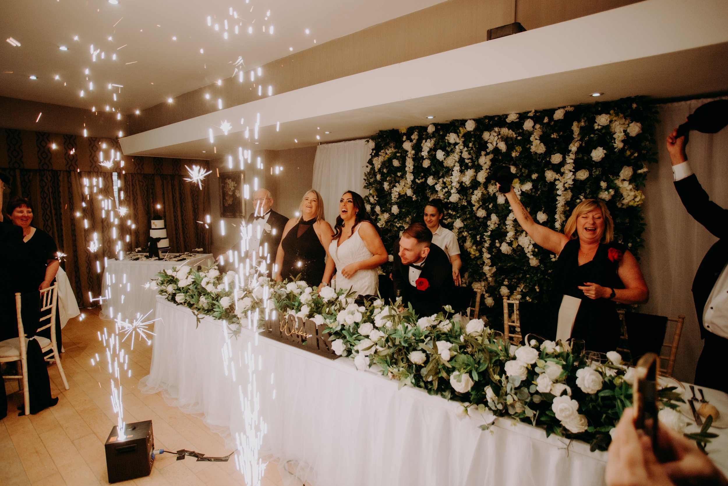 Wedding breakfast introduction with cold sparks and floral backdrop.