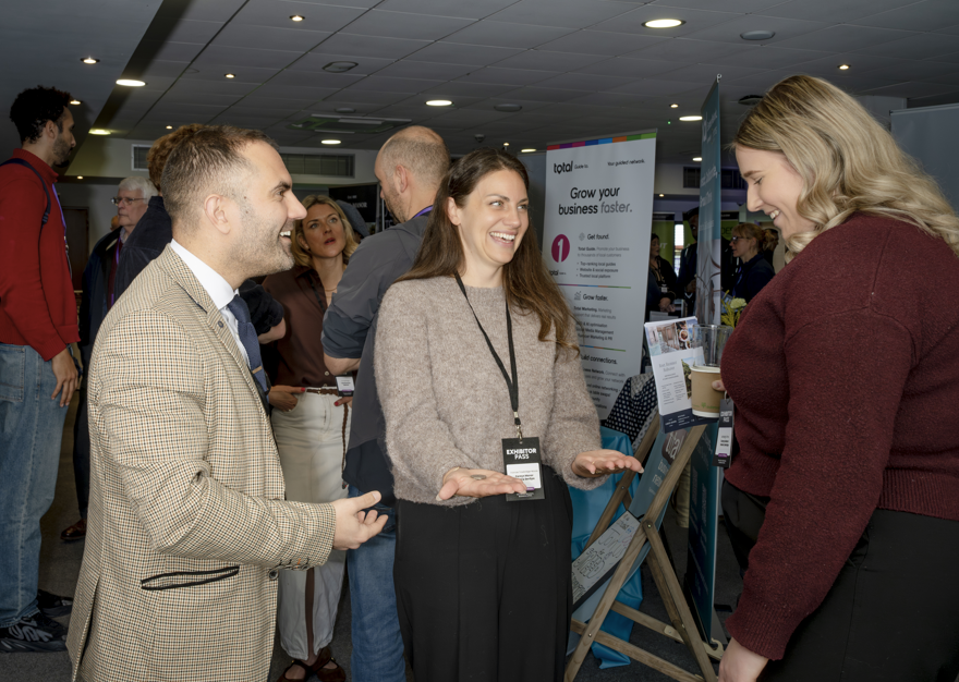 Corporate magician performing close-up magic for two women at a business exhibition