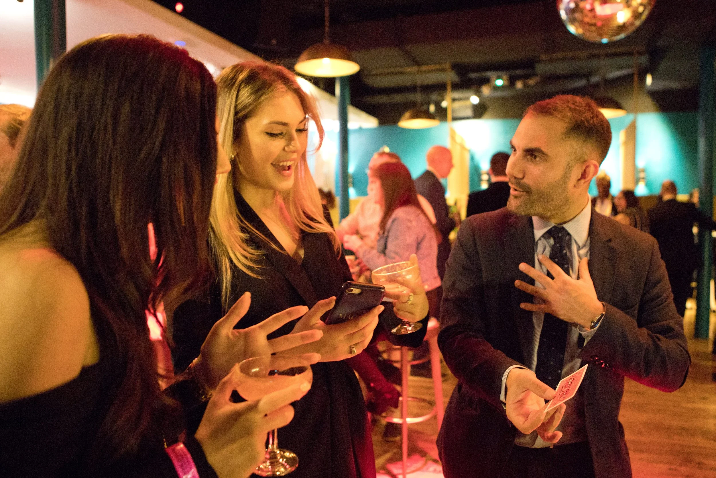 Corporate magician performing card magic for two women at a corporate drinks reception