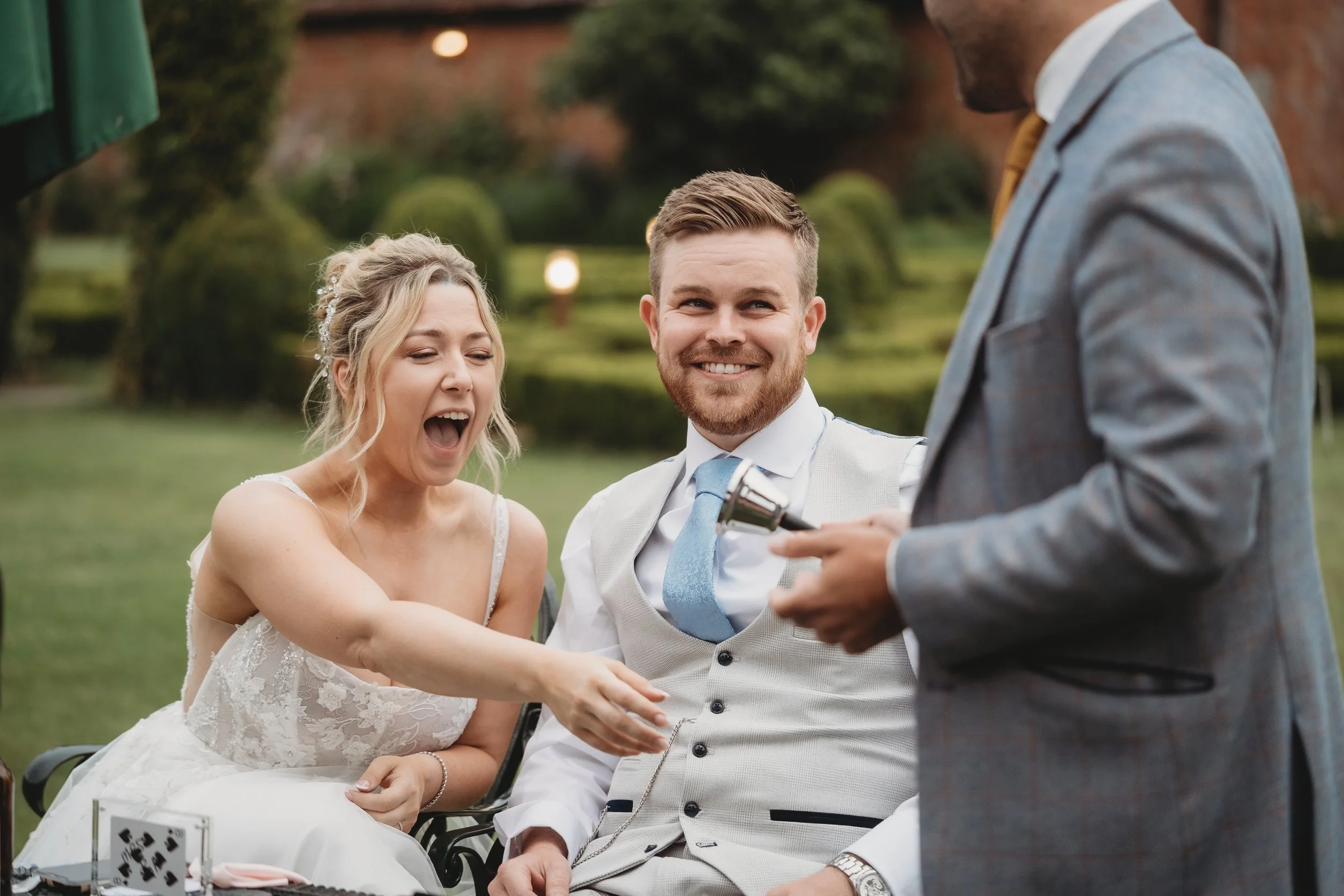Bride and groom reacting to close-up magic from wedding magician Alfie in the gardens at Parley Manor, Dorset
