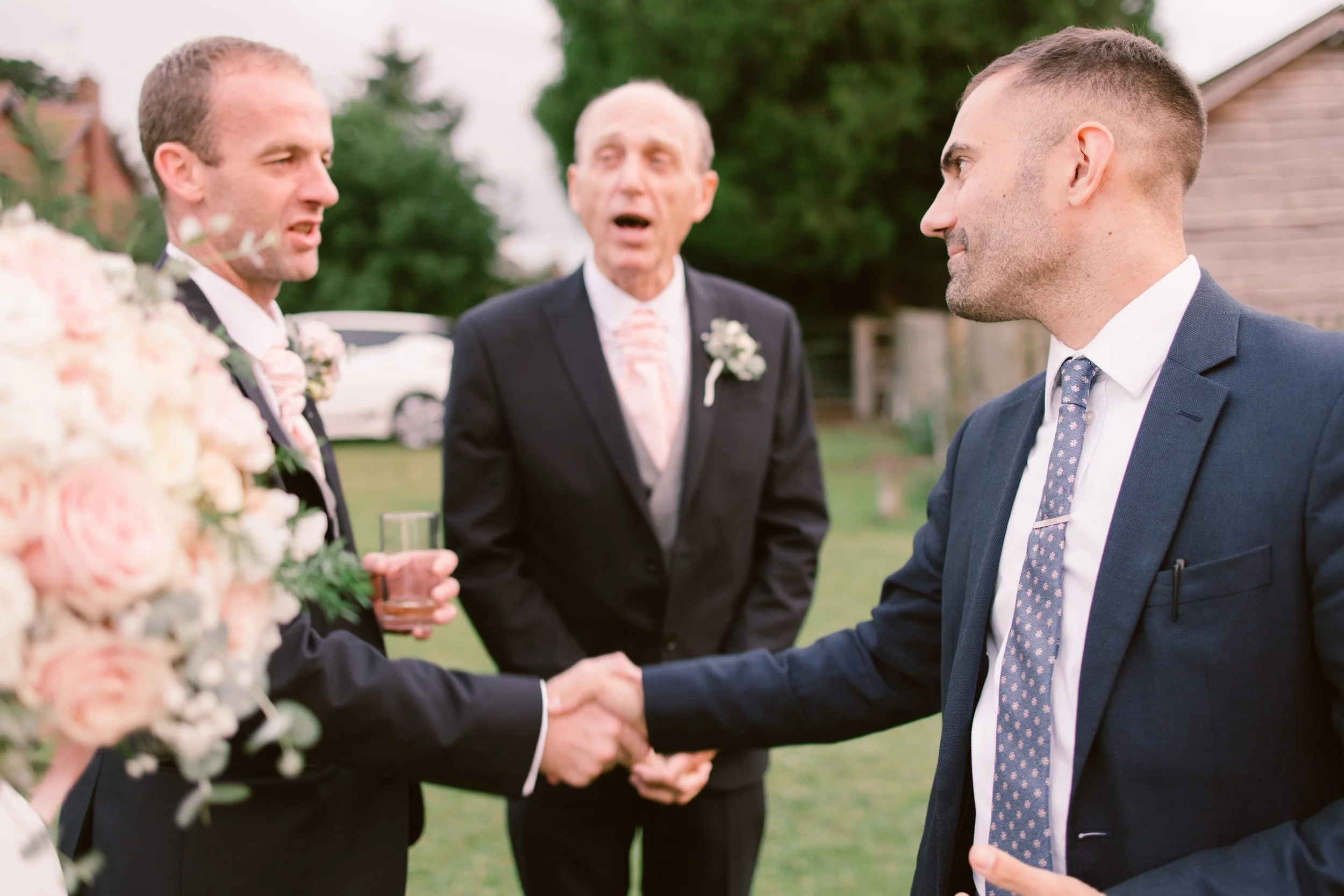 Wedding host and groom handshake on lawn
