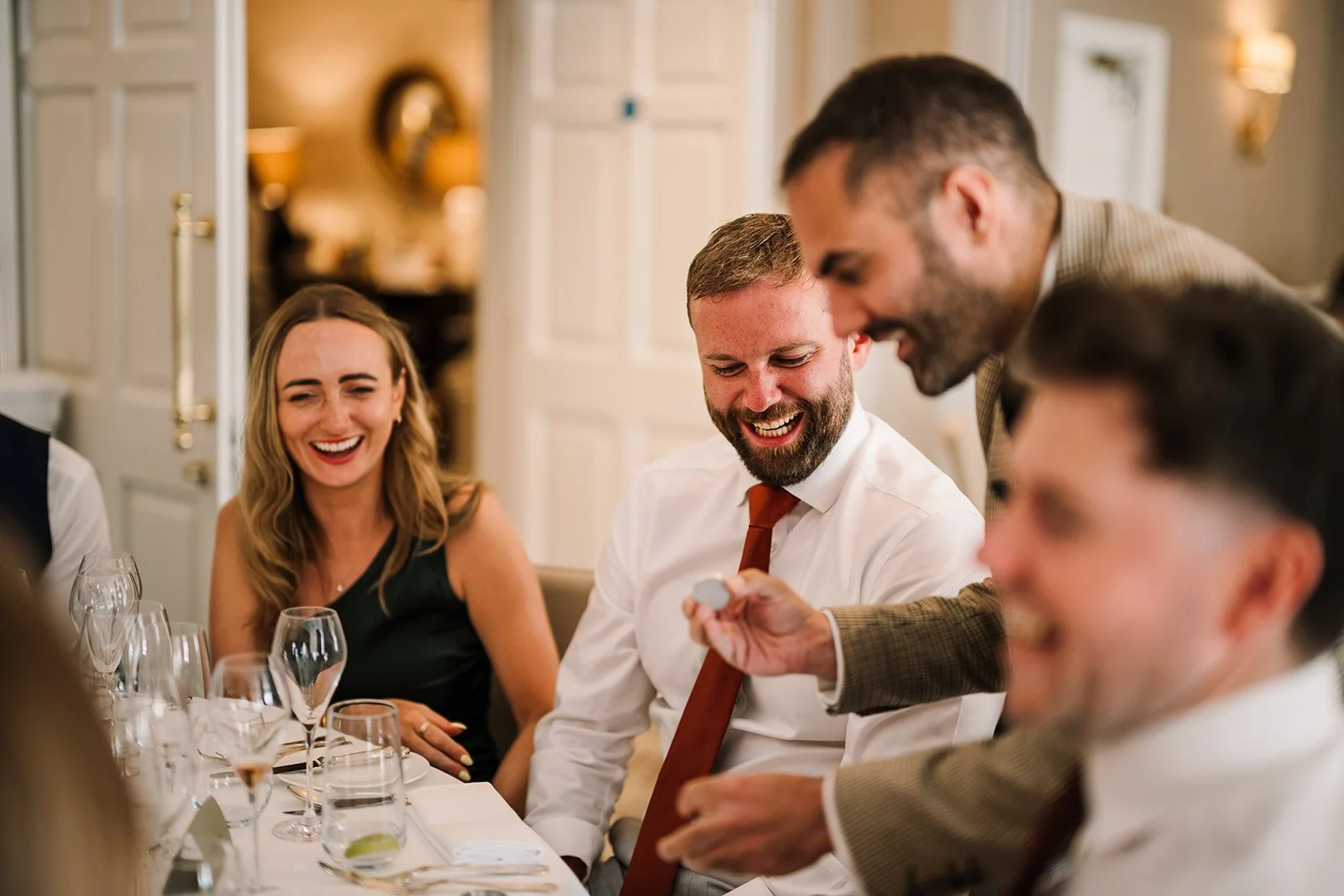 VIP event guests laughing in astonishment as a close-up magician performs a coin trick at the table