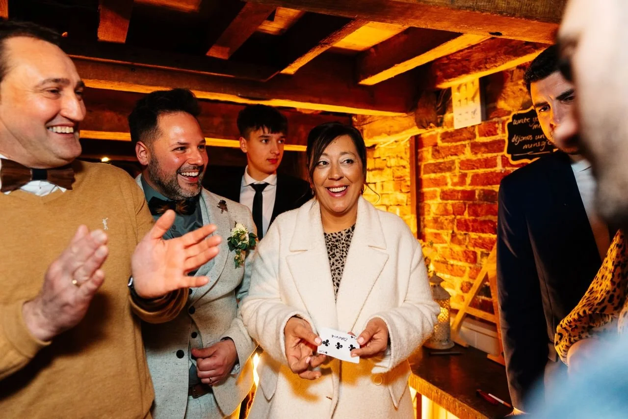 A wedding magician performs close-up magic for a group of delighted guests at a rustic barn wedding venue