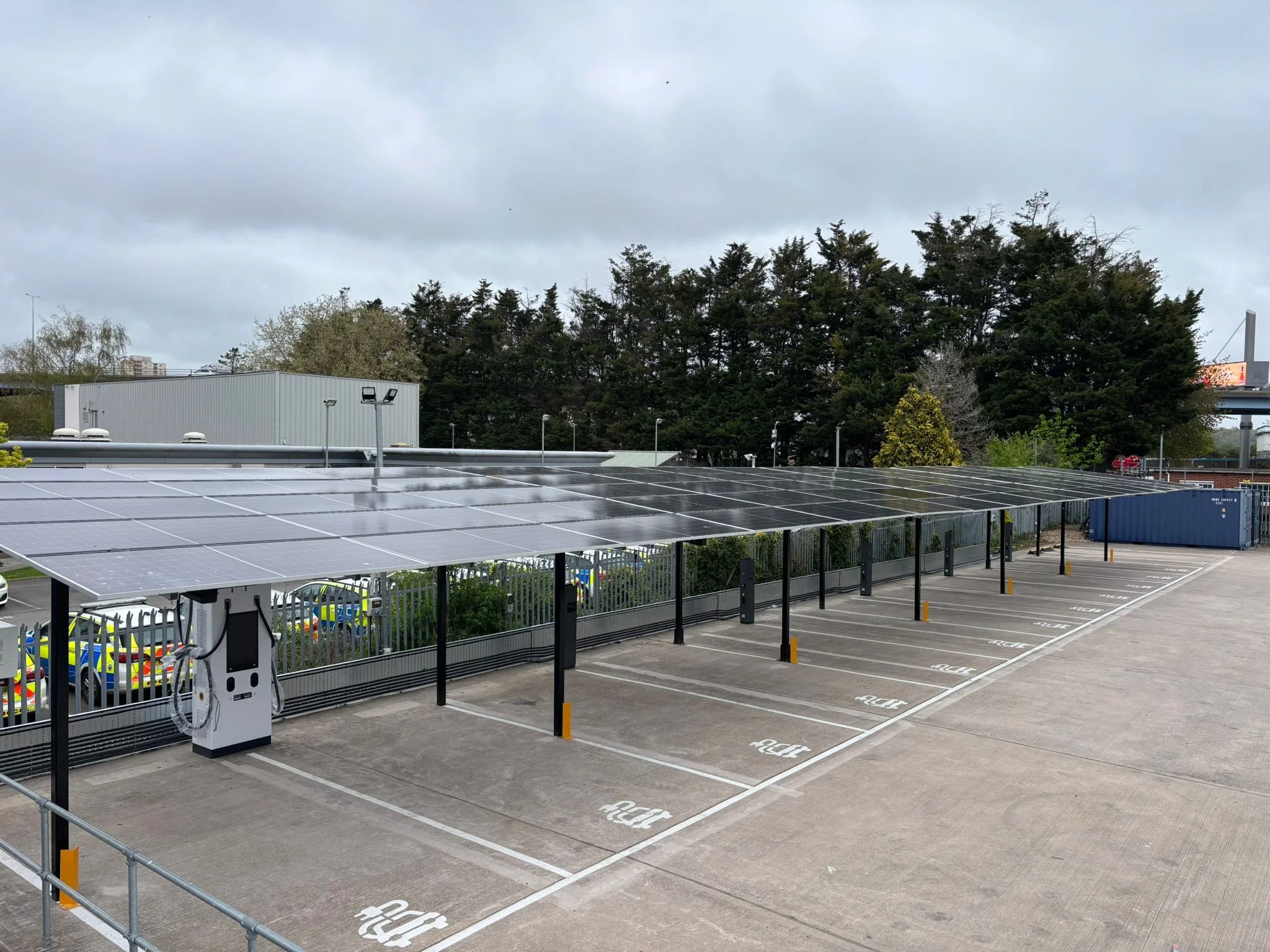 Carport with solar panels covering parked cars in a parking lot outside a warehouse