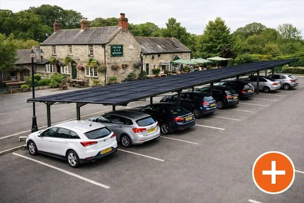 Parking lot with covered shade and several cars parked in front of a stone building with greenery.