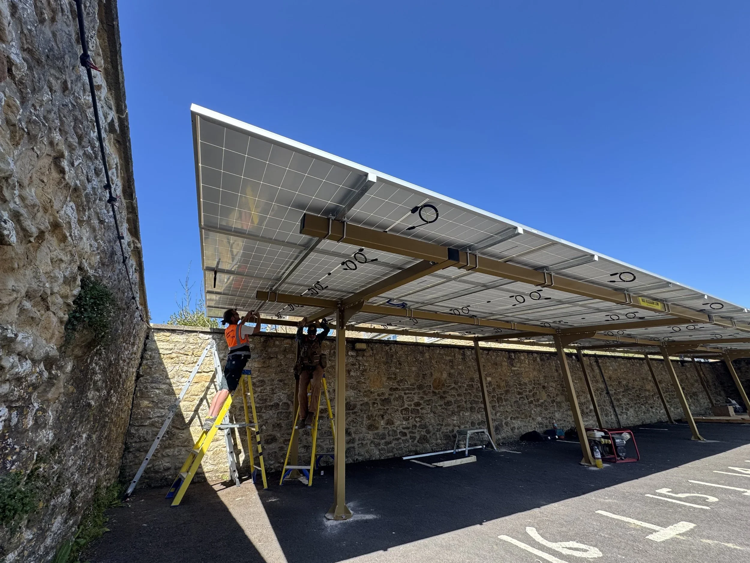 Two workers installing solar panels on a parking structure against a clear blue sky.