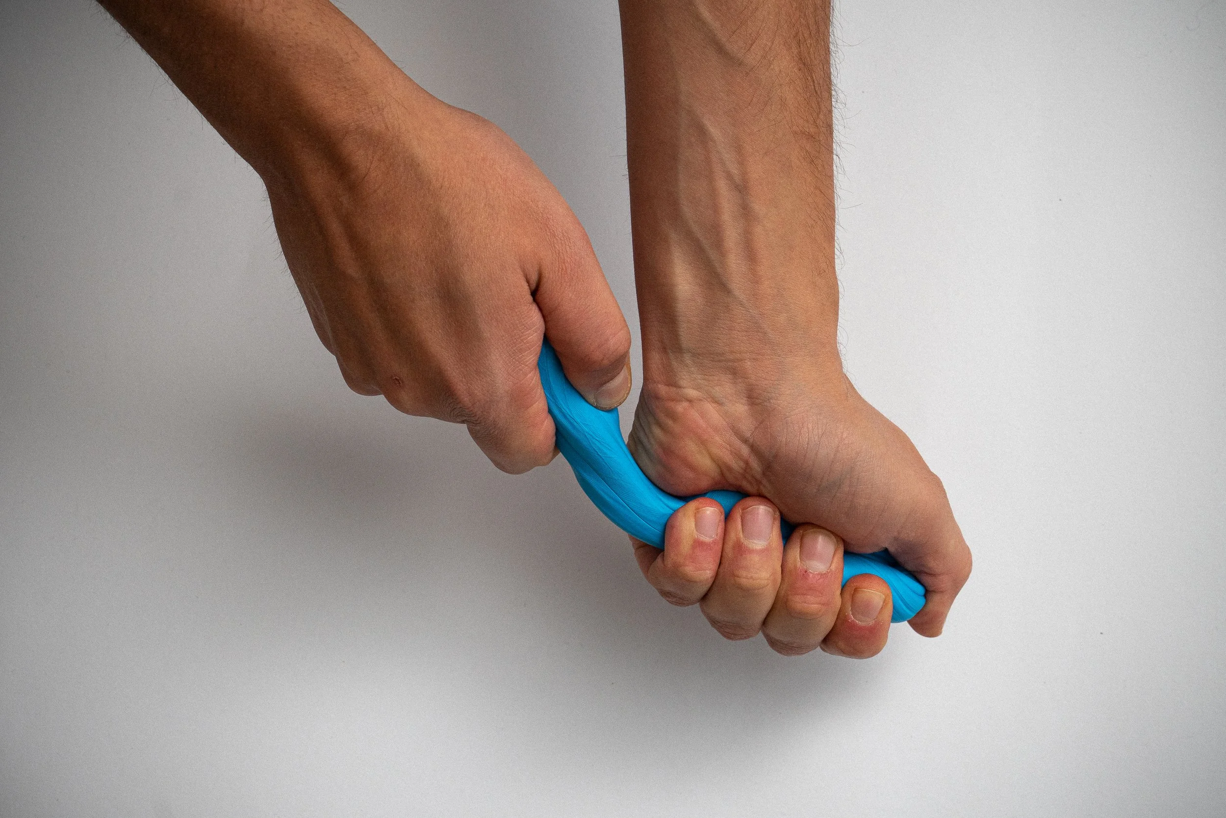 Eine Person rollt einen blauen Gummikorkenzieher zwischen den Händen auf einer weißen Oberfläche.