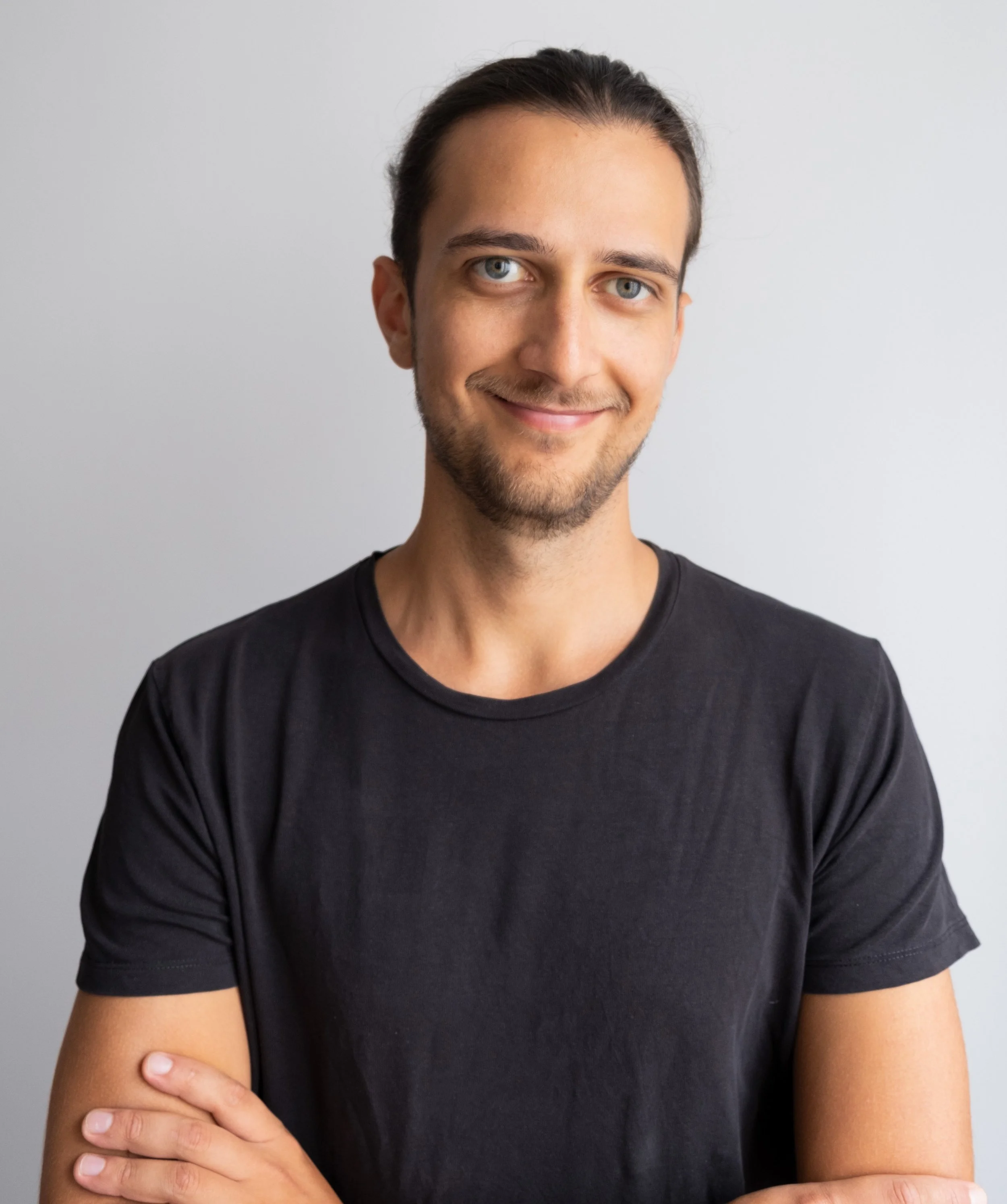 Junger Mann mit dunklem T-Shirt, lächelnd, vor hellem Hintergrund.