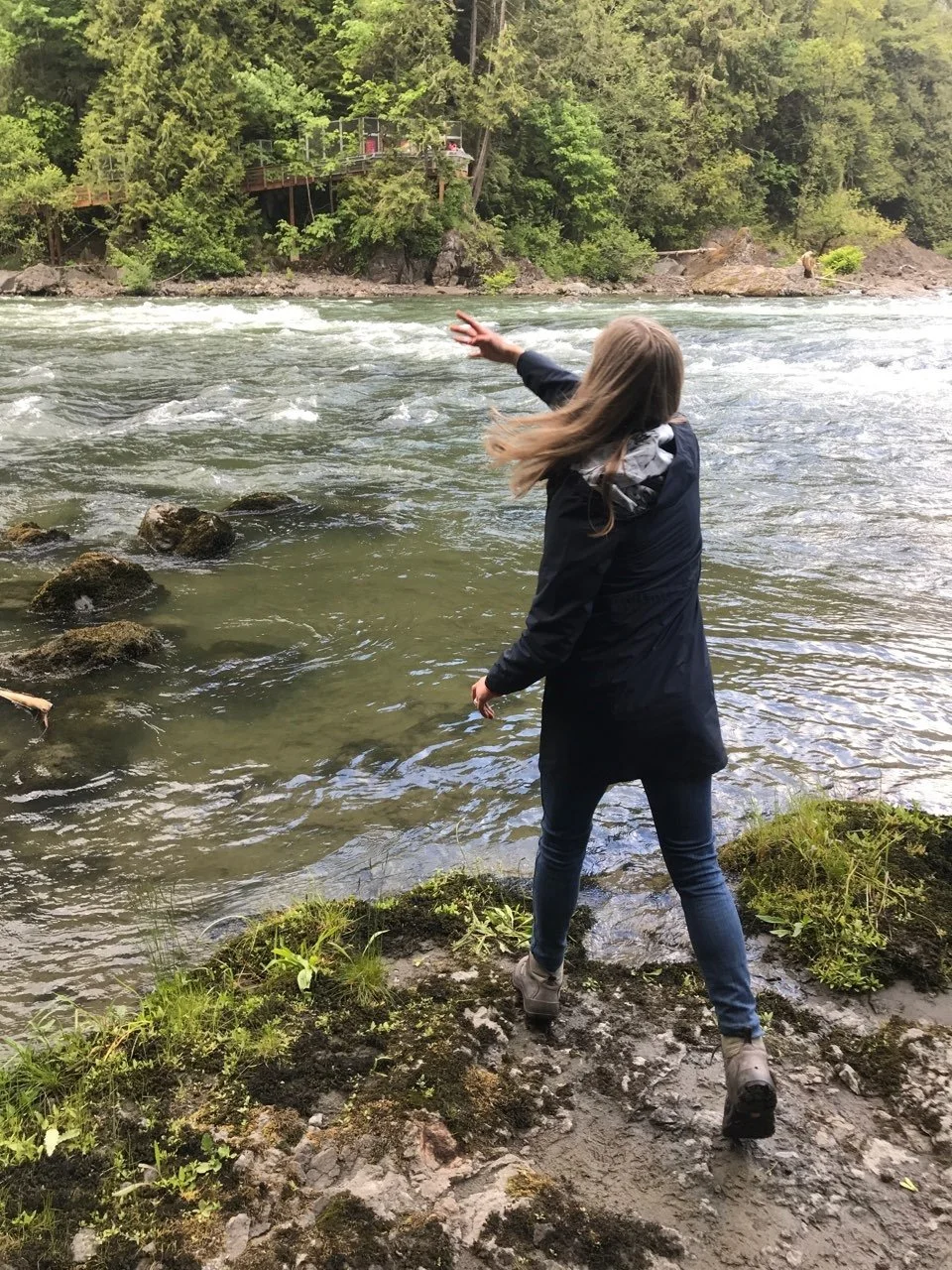 Person standing near a flowing river in the Pacific Northwest