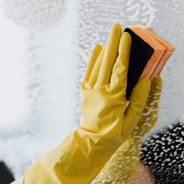 Person wearing yellow gloves cleaning a glass window with a sponge.
