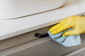 A person wearing yellow gloves cleaning a drawer handle with a cloth.