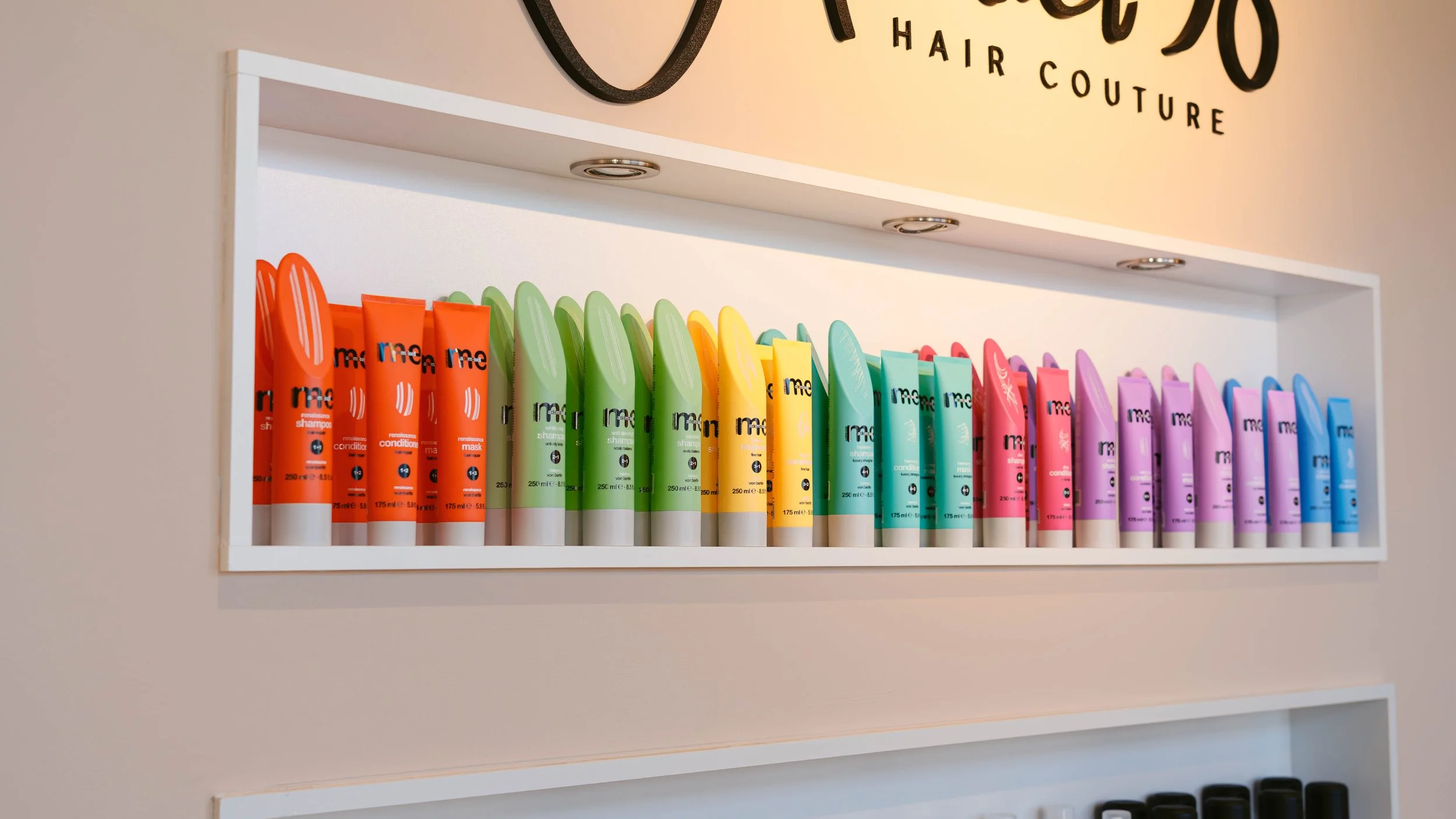 Regal mit bunten Flaschen von Haarpflegeprodukten in den Farben Rot, Grün, Gelb, Türkis, Pink und Blau, in einem Friseursalon.