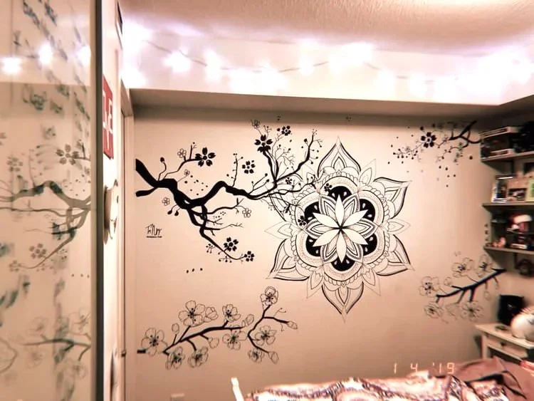 Black and white mural of a tree branch with blossoms and a detailed mandala design on the wall.