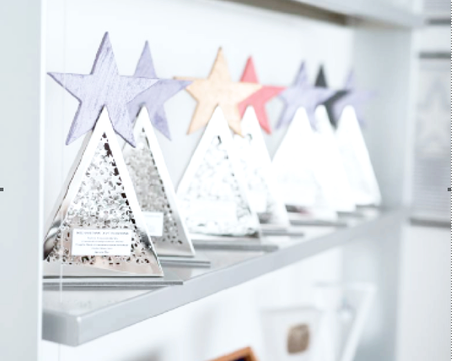 Decorazioni natalizie a forma di alberi con stelle colorate sulla sommità, esposte su una mensola