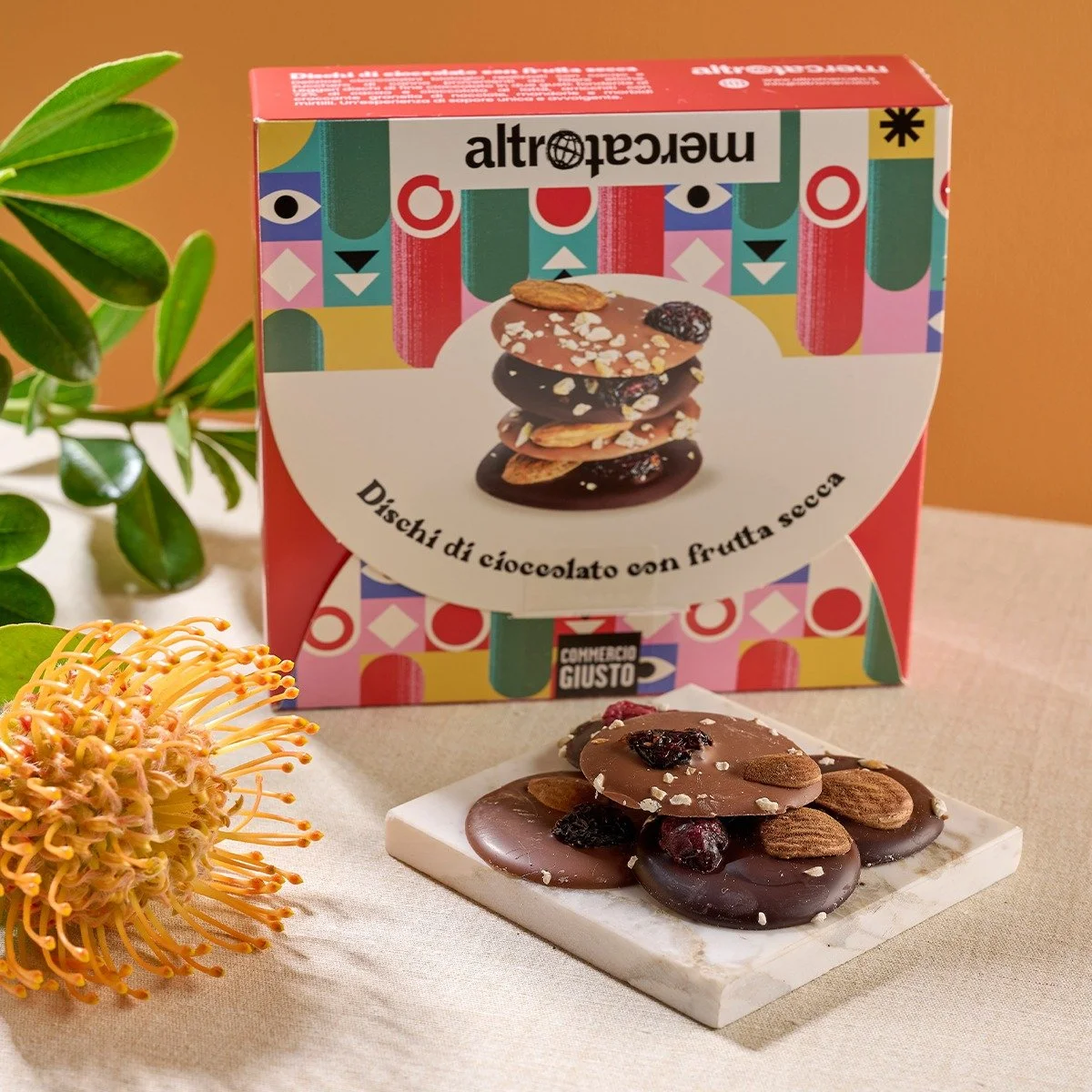 Set di dischi di cioccolato con frutta secca, mele e uvetta, posti su una base di marmo altromercato, mercato equosolidale, sostenibilità, food packaging