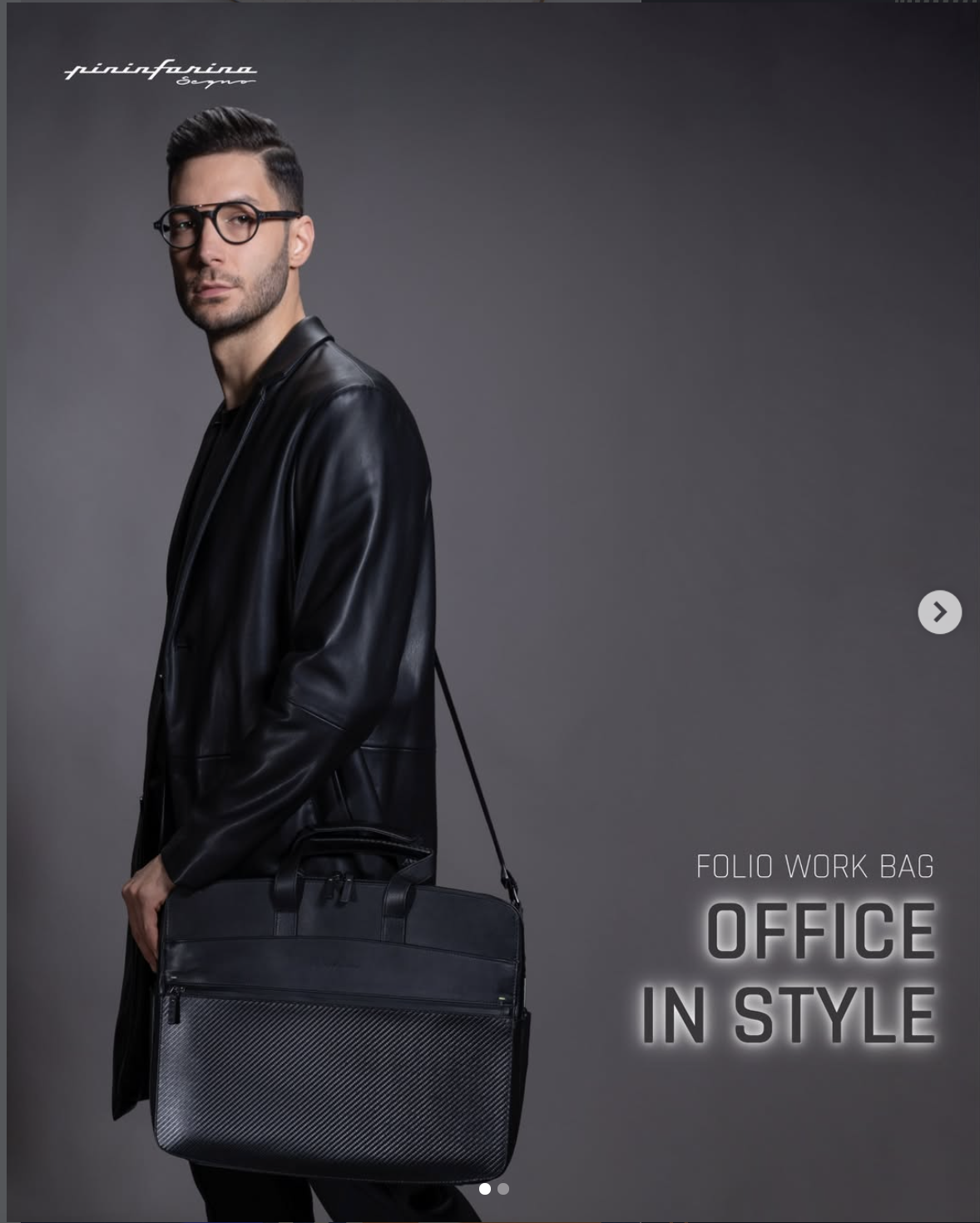 Uomo con occhiali e capigliatura ben curata, indossa una giacca in pelle nera e tiene una valigetta da lavoro nera con dettagli geometrici, sfondo grigio scuro.