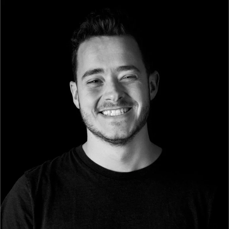 Ragazzo sorridente con barba, capelli corti e vestito nero, sfondo nero