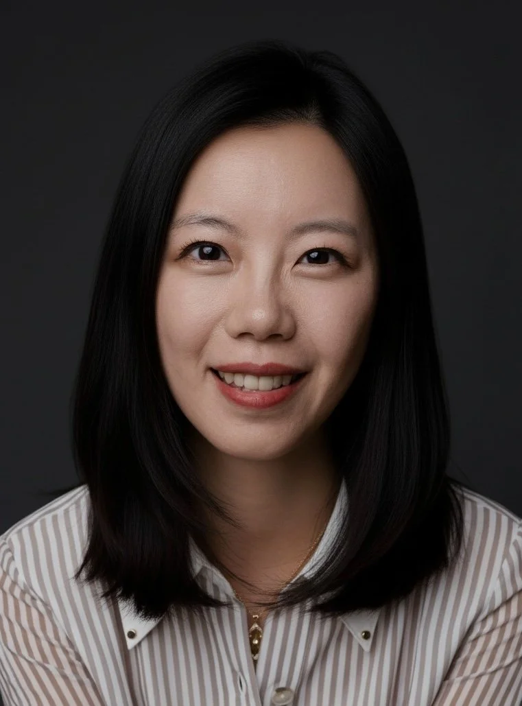 Close-up portrait of a woman with black hair, smiling, wearing a white striped shirt, against a dark background.