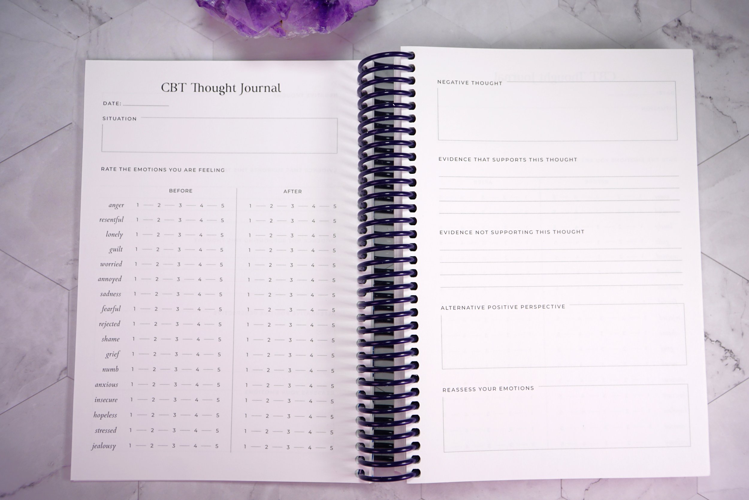 Open CBT Thought Journal with space for date, situation, emotion ratings, and areas for reflecting on negative thoughts, evidence, alternative perspectives, and re-interpretation, on a marble surface.