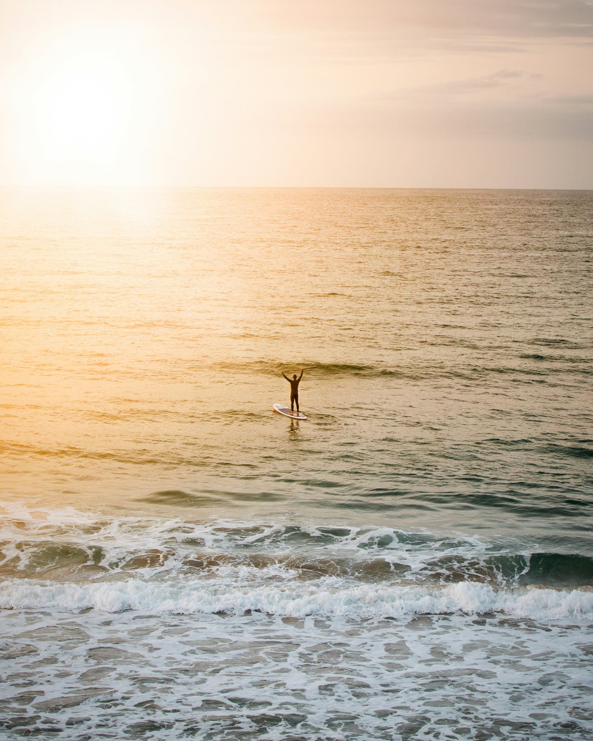 Person stand-up paddleboarding on the ocean during sunset