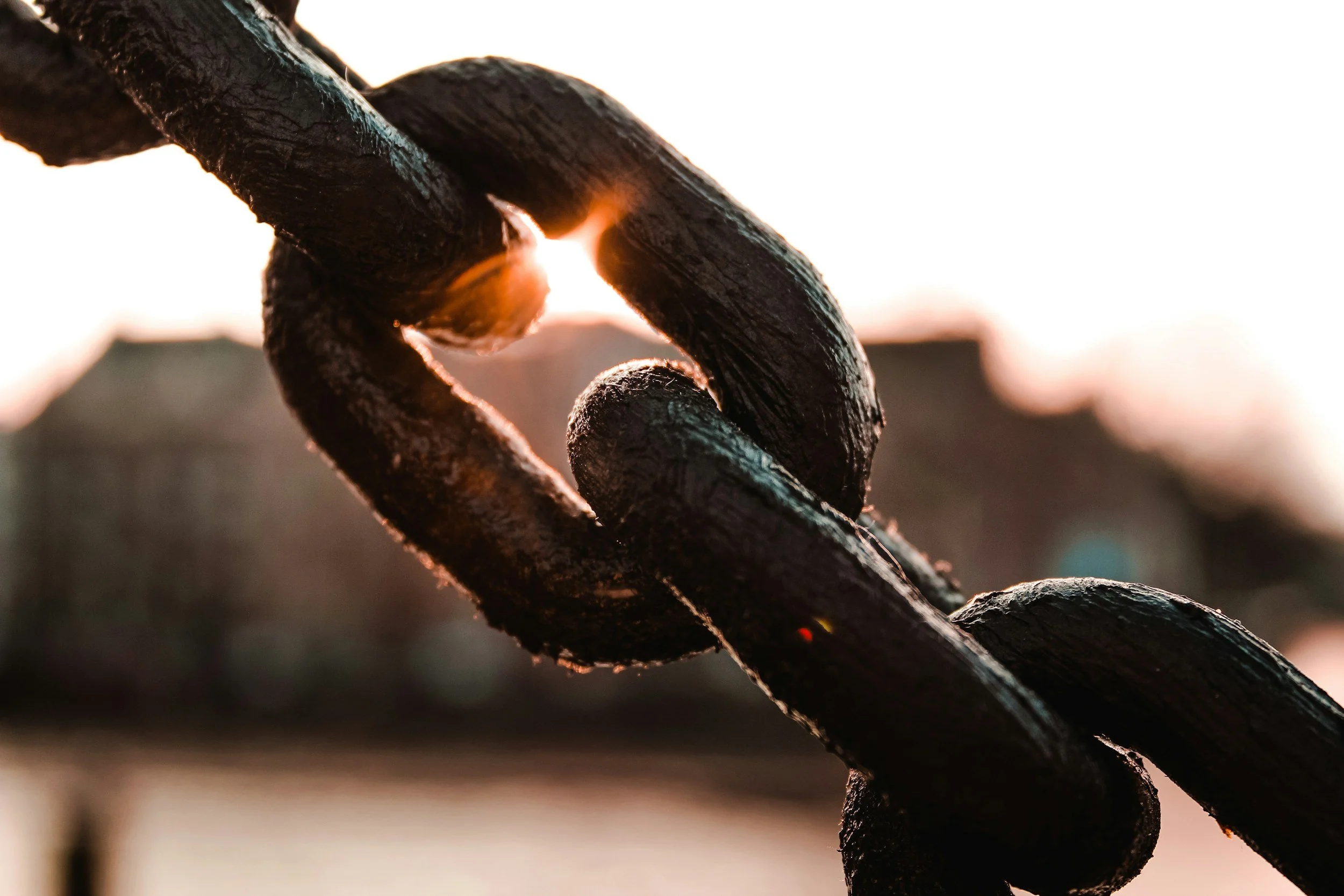 Close-up of a black metal chain link with the sun setting in the background.