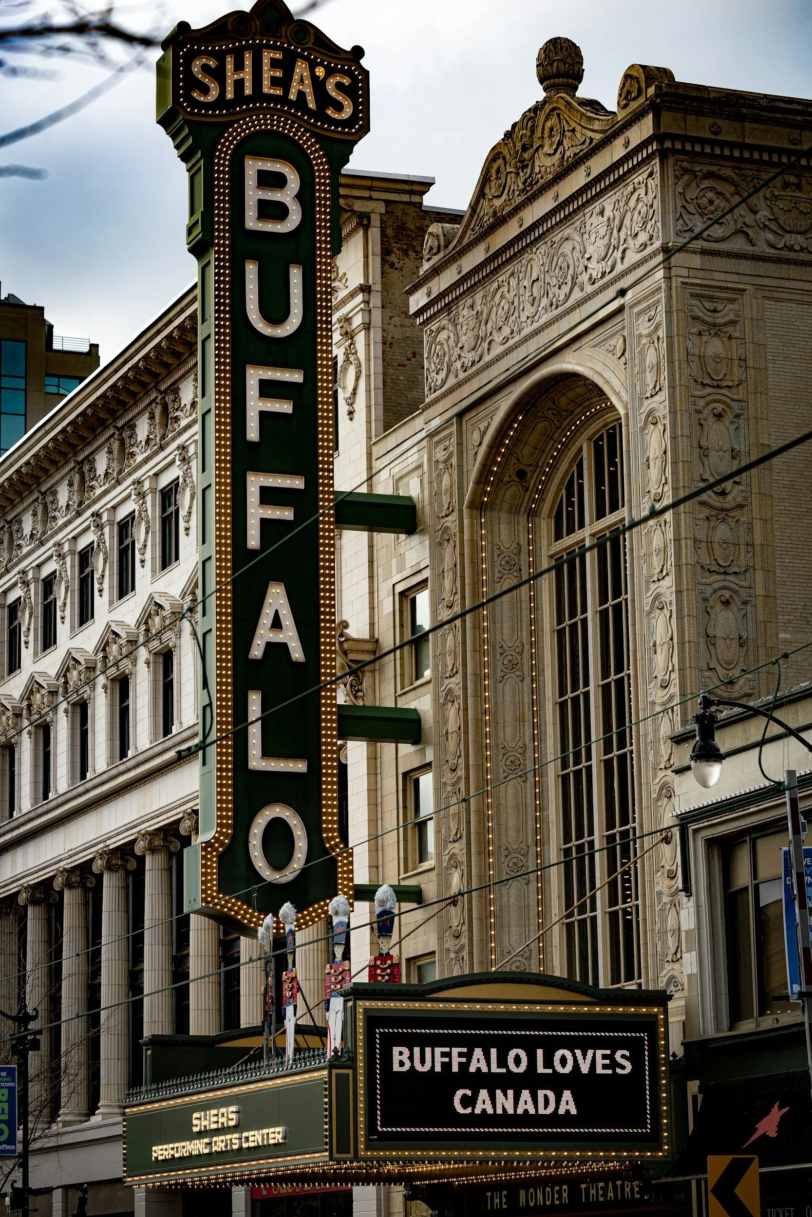 The Sheas Buffalo marquee sign on a historic building, with the text 'BUFFALO LOVES CANADA' displayed on a digital board below, and decorative Nutcracker figures on the building's facade.
