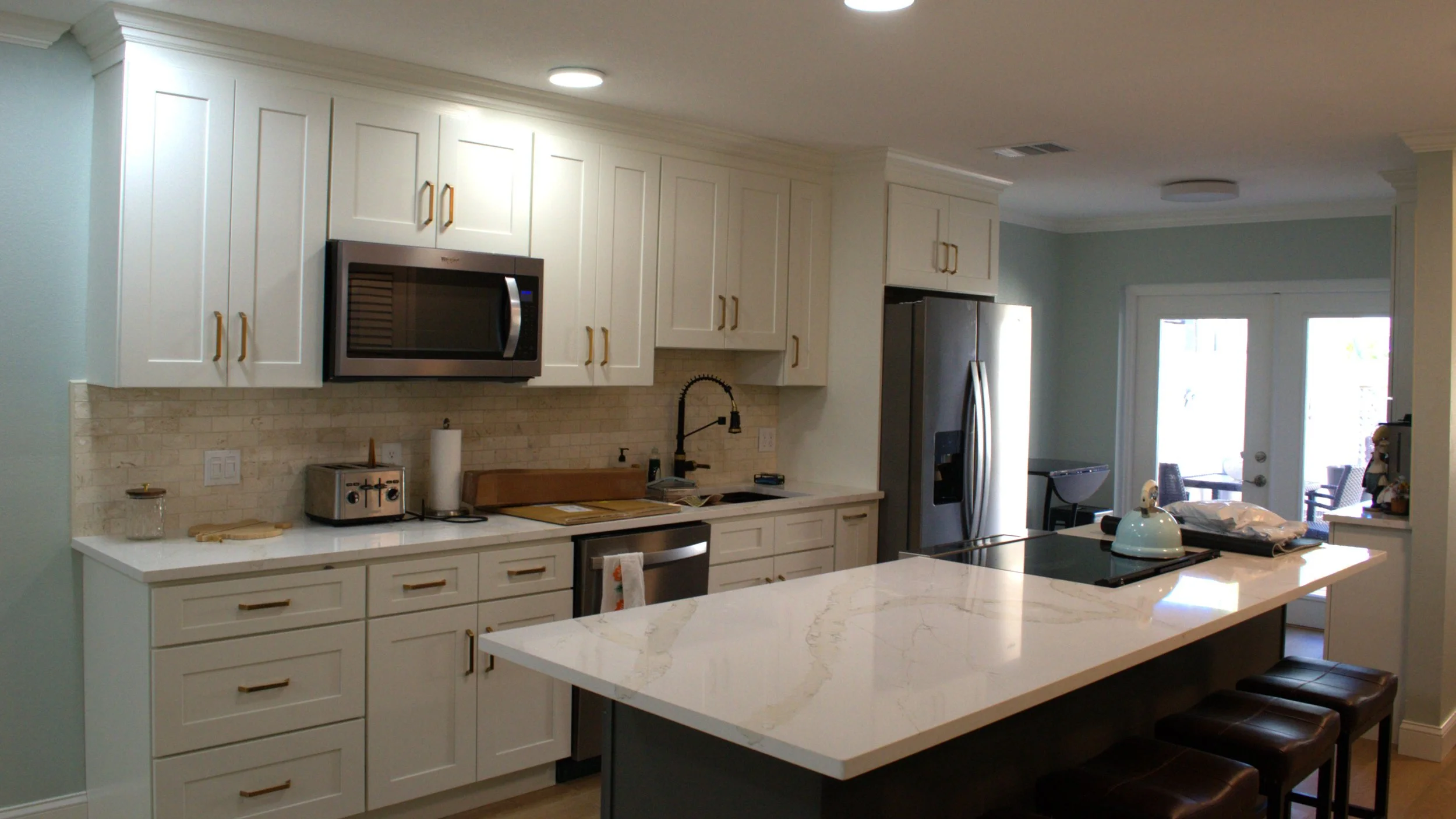 Modern kitchen with white cabinets, stainless steel appliances, marble countertop island, and natural light from a glass door leading outside