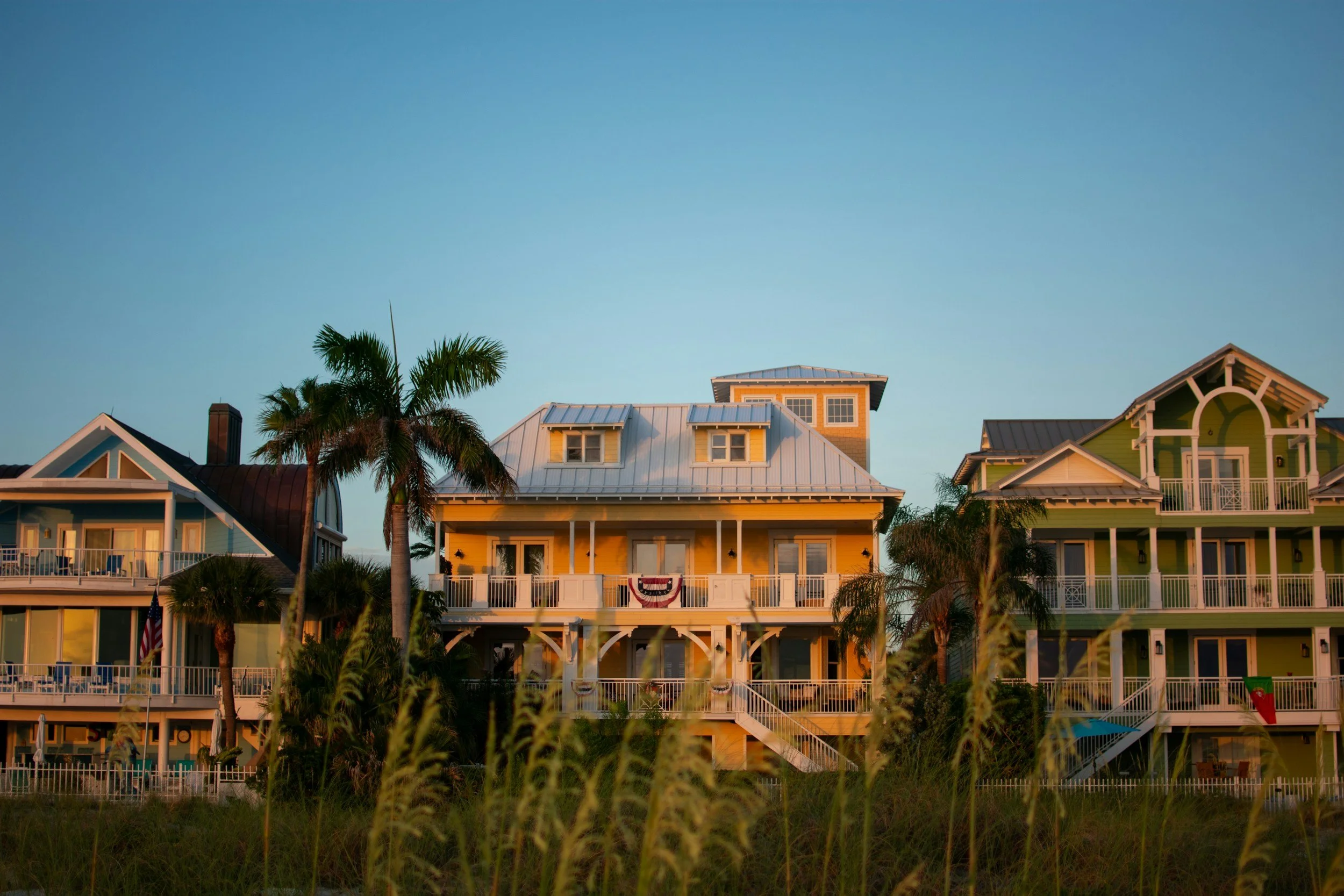 Colorful beach houses with balconies and palm trees, under a clear sky.