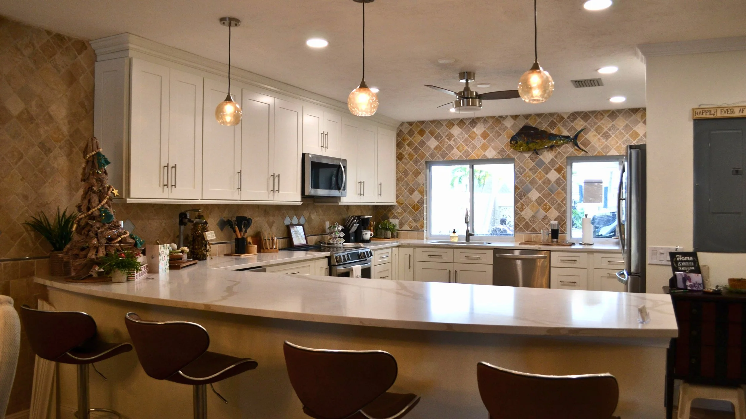 Modern kitchen with white cabinets, beige tile backsplash, marble countertop, stainless steel appliances, and bar seating.