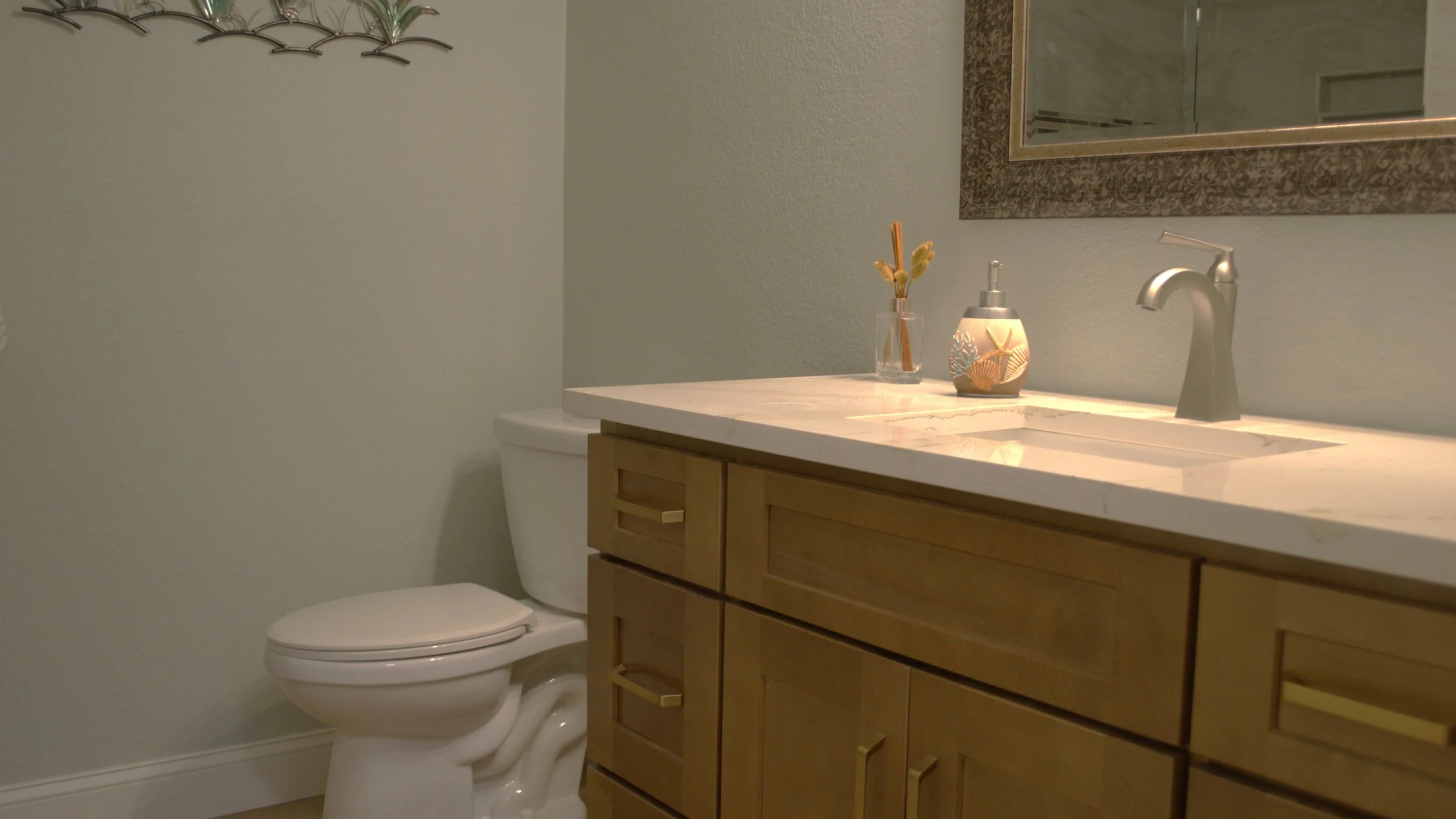 Bathroom with toilet and wooden vanity with marble countertop, decorative items, and a mirror.