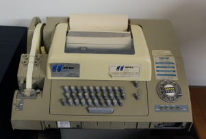 A photo of a cream and green telex machine on a wooden desk