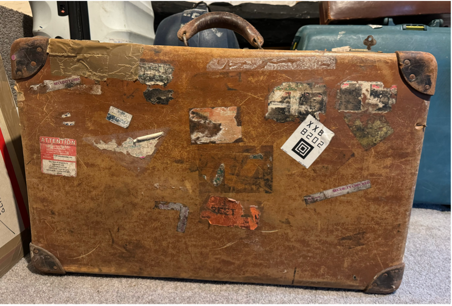 an old brown suitcase standing upright covered in worn travel stickers